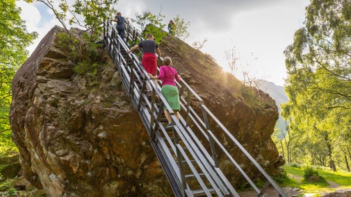 Three people walking up the steps into a large boulder at the Bowder Stone in Cumbria